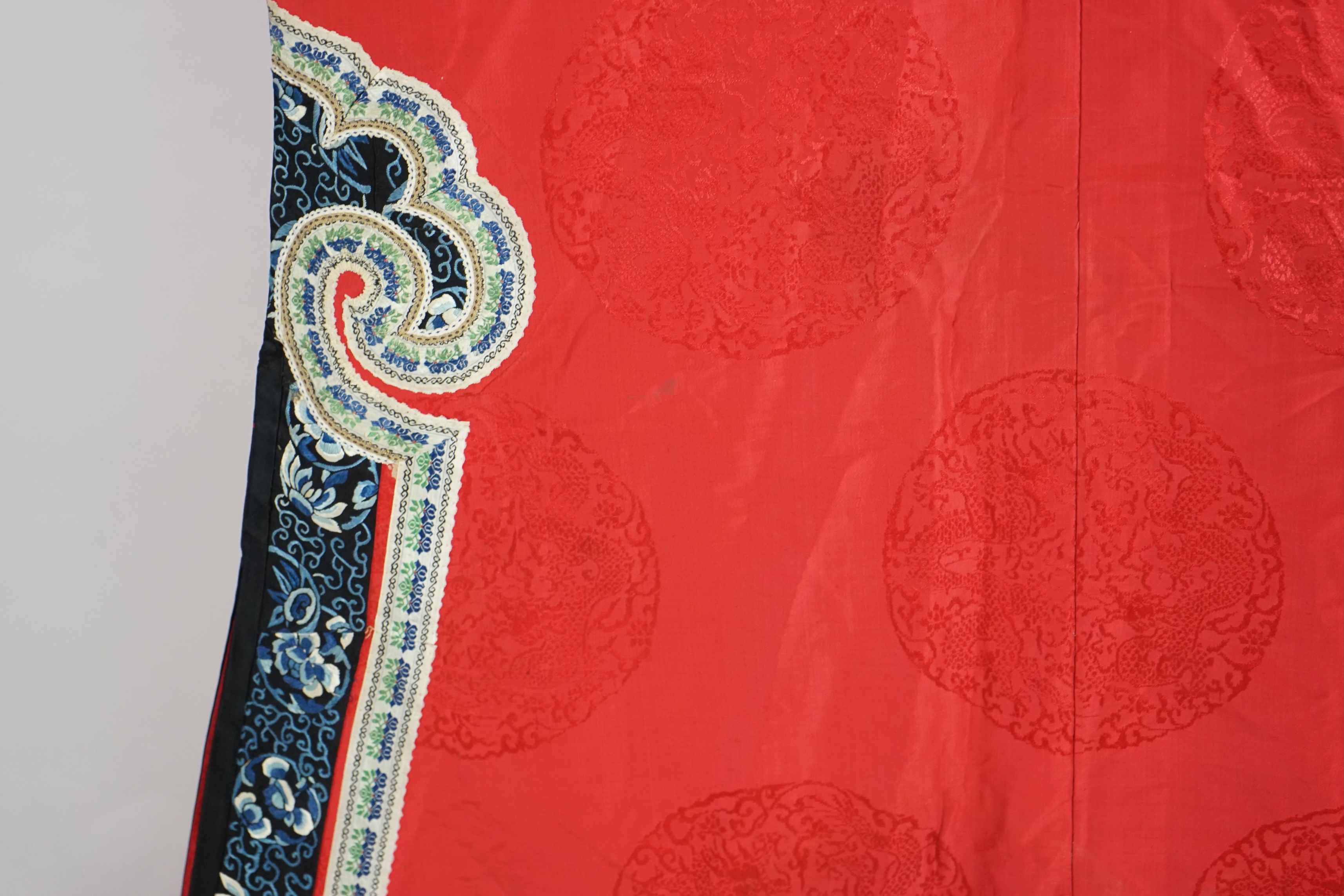 A late 19th century Chinese Manchu ladies red silk damask robe, with black and blue silk embroidered borders, ornately edged cream floral silk braiding, length from neck (back) to bottom edge 132cm long. Condition - stai